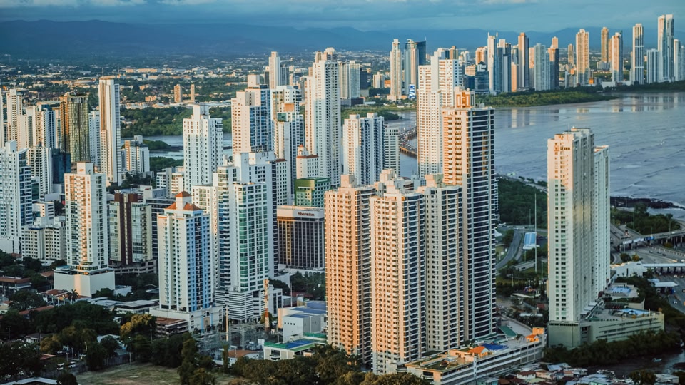 Cluster of high-rise towers beside a bay in Panama City with sunlight on glass facades.