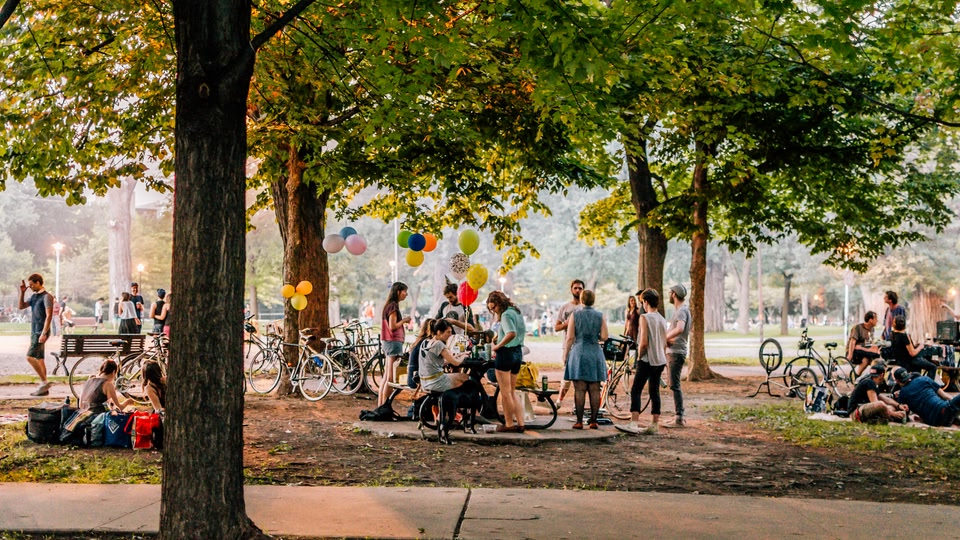 A group of people gathered in a park with balloons and bicycles, suggesting a festive atmosphere.