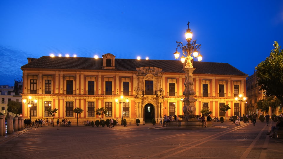Illuminated historic building at night with people walking around in the courtyard.