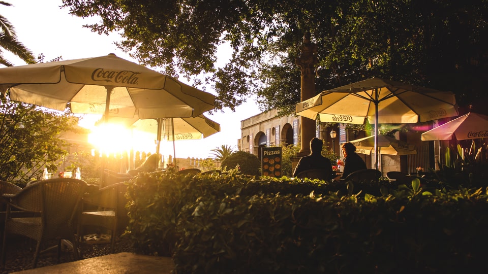 People sitting under umbrellas at an outdoor café as the sun sets.