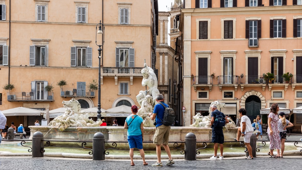 Tourists standing in front of a large baroque fountain in Piazza Navona, Rome.