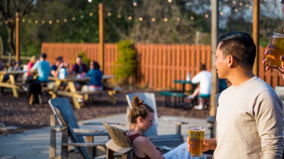 A group of people socializing at an outdoor bar in Charlotte, North Carolina, with one man holding a glass of beer.