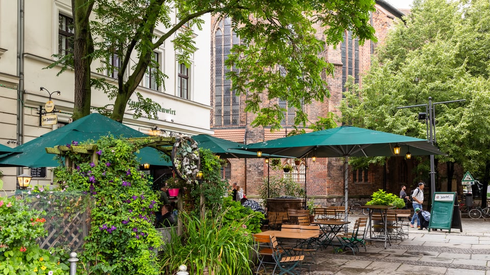 Outdoor seating area of a cafe with green umbrellas, tables, chairs, and lush greenery.