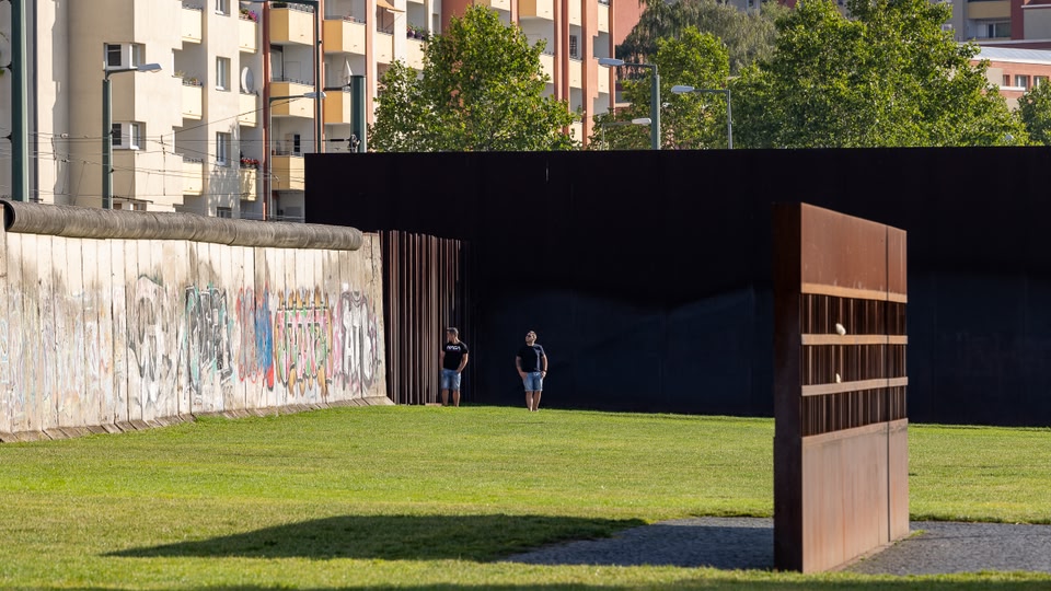Two people standing in front of a black wall with graffiti at the Berlin Wall Memorial in Berlin, Germany.
