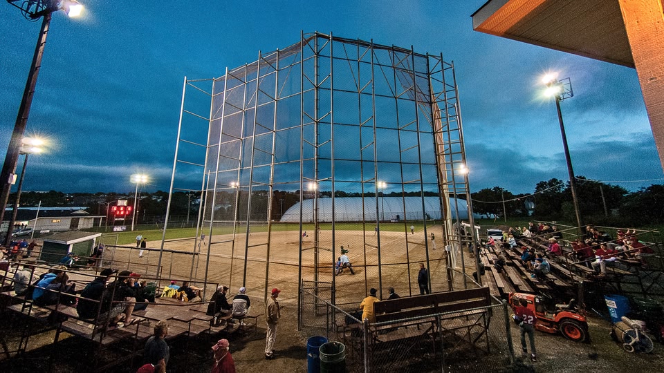 A night baseball game with spectators in the stands and players on the field.