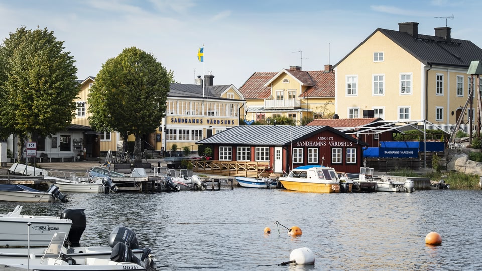 View of boats docked at a waterfront with yellow buildings and a Swedish flag in the background.