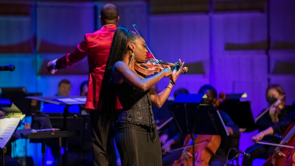 A violinist performs on stage in front of an orchestra during a concert.
