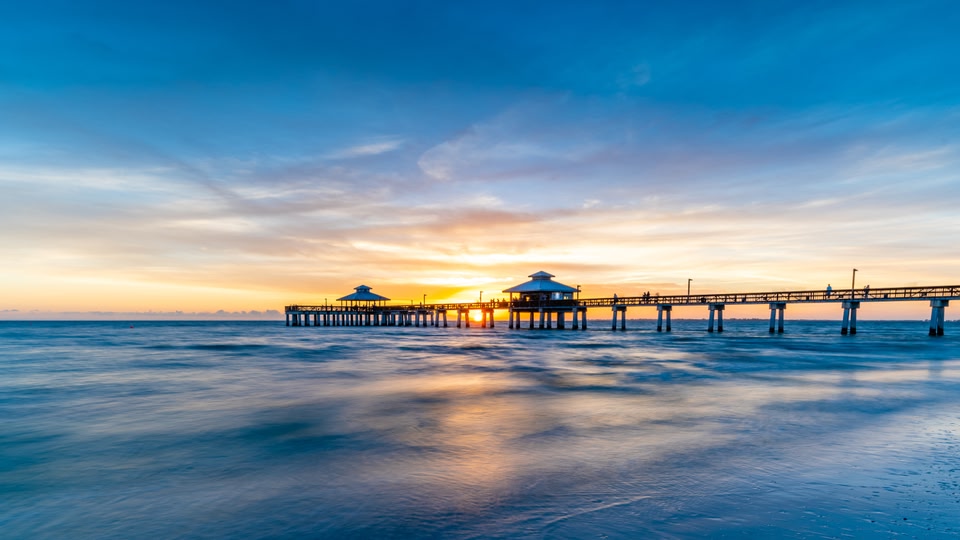Sunset over a pier with the sun setting in the background, casting a warm glow over the water and sky.