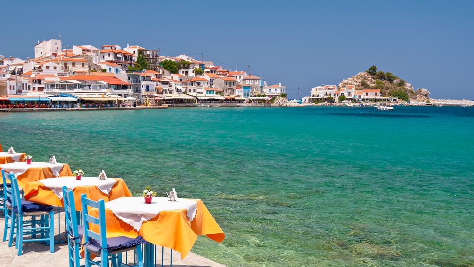 Aerial view of a coastal town with red-roofed buildings and a marina full of sailboats.