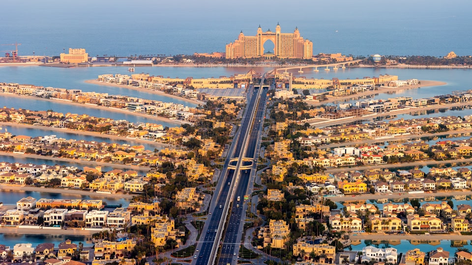 Aerial view of The Palm Jumeirah in Dubai showing extensive urban development, the iconic Atlantis hotel, and the surrounding water channels.
