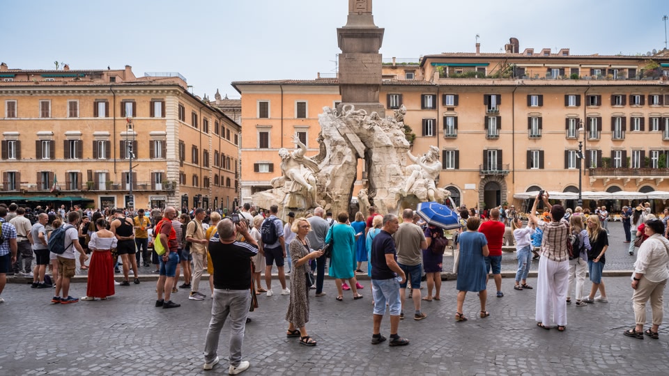 A crowd of people gathered around a historic monument in Piazza Navona, Rome.