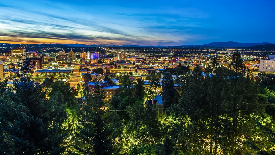 A panoramic view of a city skyline at dusk with warm lighting and a blue sky transitioning into night.