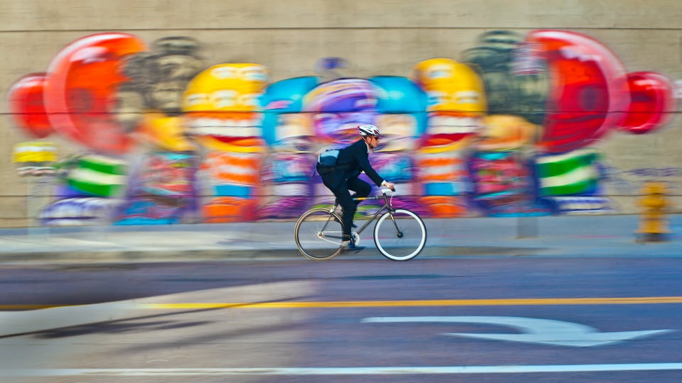A cyclist rides quickly past a colorful mural on a city street.
