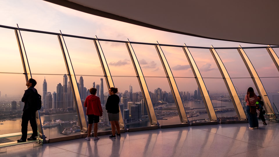 People standing in front of a glass wall overlooking a city skyline at dusk.