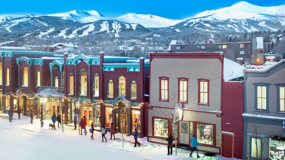 A snowy street in Breckenridge, Colorado, with people walking and shops decorated with lights.