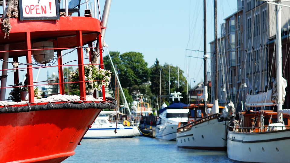 A close-up view of the bow of a red boat labeled 'OPEN!' docked at a waterfront, surrounded by other boats and buildings.