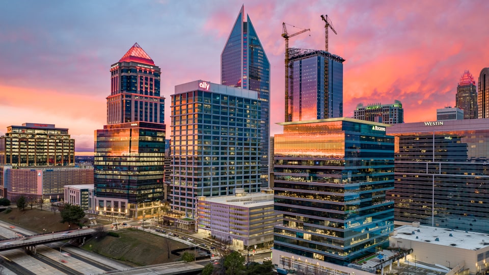 A cityscape of Charlotte, North Carolina, during sunset with illuminated buildings and a colorful sky.