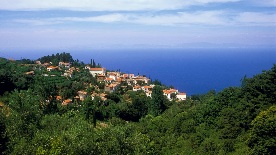 Aerial view of a hillside village in Samos, Greece, with the ocean in the background.