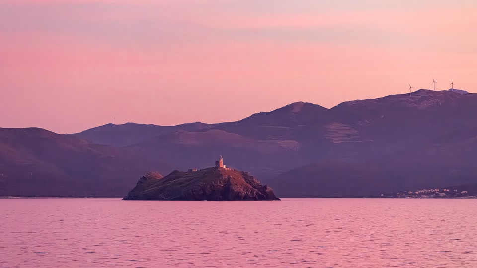 Rocky islet with a lighthouse at dusk, pastel purple-pink sky and calm sea in Cap Corse.