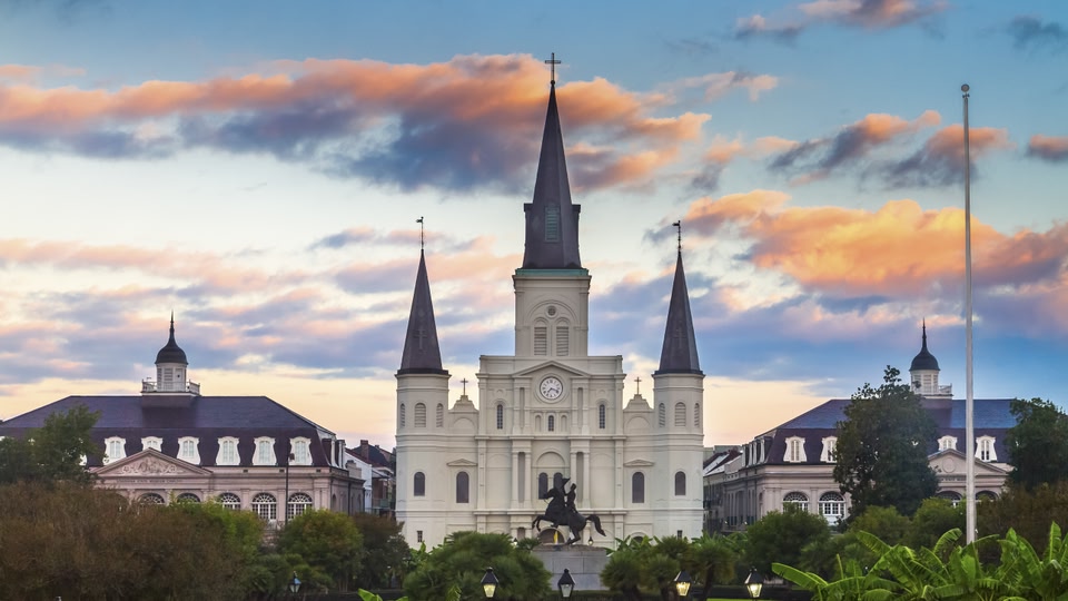 A historical church in New Orleans at sunrise or sunset with vibrant orange and pink clouds.
