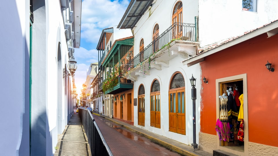 Sunlit colonial street with balconies and a clothing shop in Panama City.