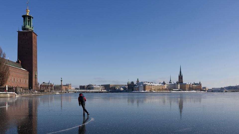 A person skating on a frozen lake in Stockholm with the city skyline in the background.