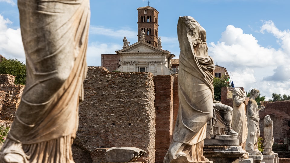 Statues and ruins at the Roman Forum in Rome, Italy, with a church visible in the background.