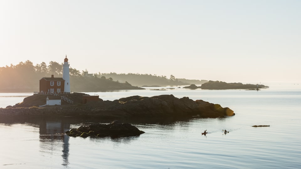 A lighthouse on a small island with two kayakers paddling in the water during sunset.