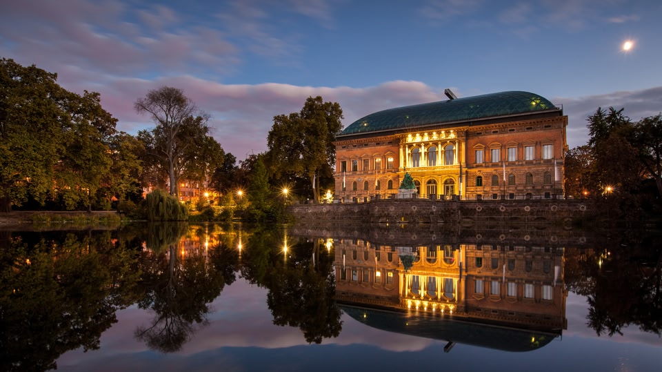 Illuminated historic building reflecting in a calm lake at night.