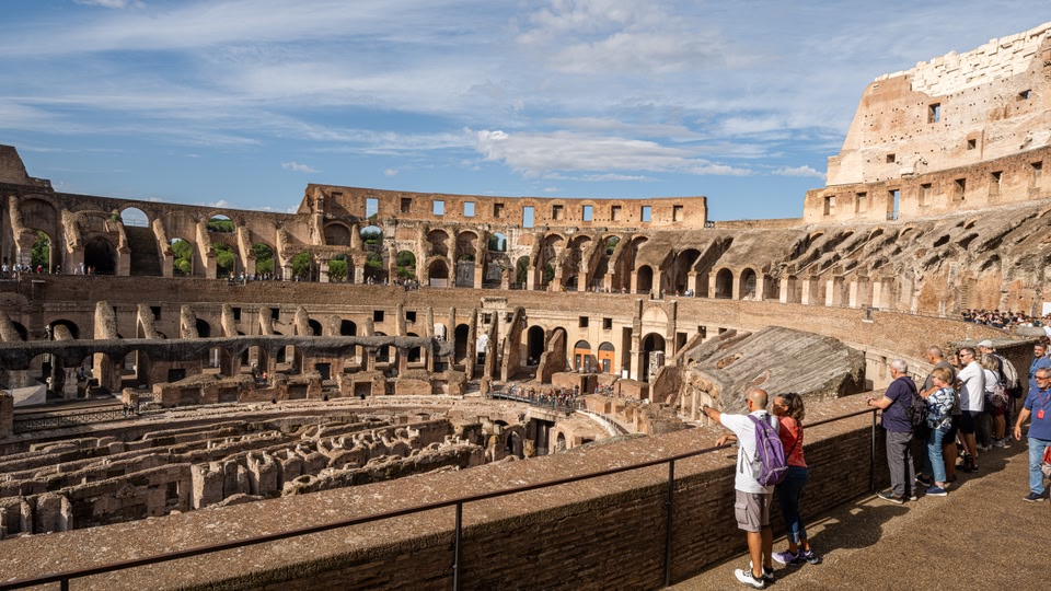 Tourists standing on the upper level of the Colosseum, Rome, looking down at the ancient amphitheater.